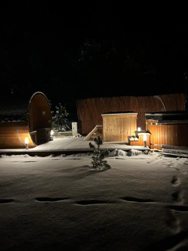 un patio cubierto de nieve por la noche con un edificio en Domki trzy jeziora z zewnętrznym SPA - sauna, balia do schładzania i jacuzzi, en Małe Swornigacie