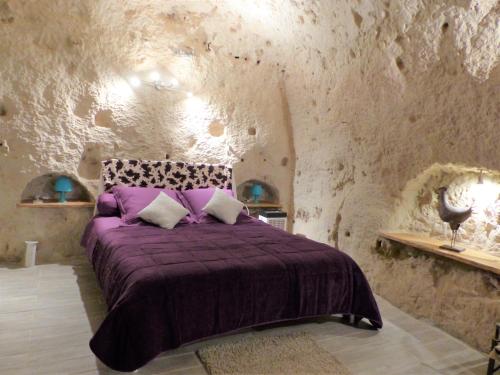 um quarto com uma cama roxa numa parede de pedra em Troglogîtes de la Tourette em Les Roches-lʼÉvêque