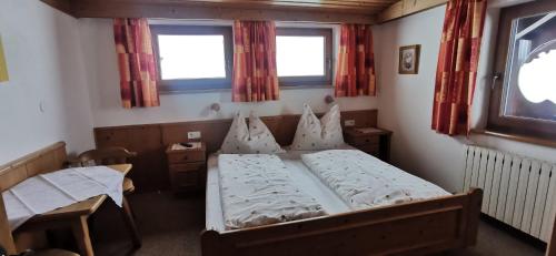 a bedroom with a bed and a table and two windows at Landhaus Stöckl in Finkenberg