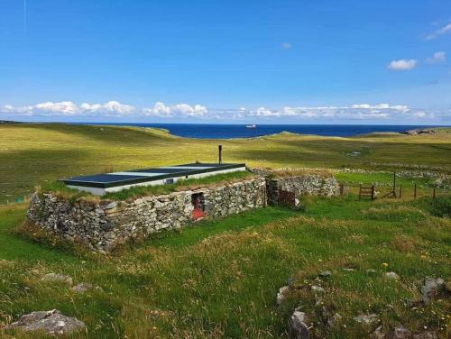 an old stone building in a field with the ocean at Squealing Pig Bothy in Bragor