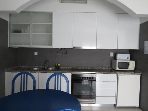 a kitchen with white cabinets and a table and a microwave at Hotel Apartamento Praia Azul in Santa Cruz