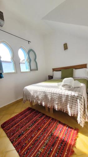 a bedroom with a bed with a rug and two windows at Honey Suckle in Chefchaouene