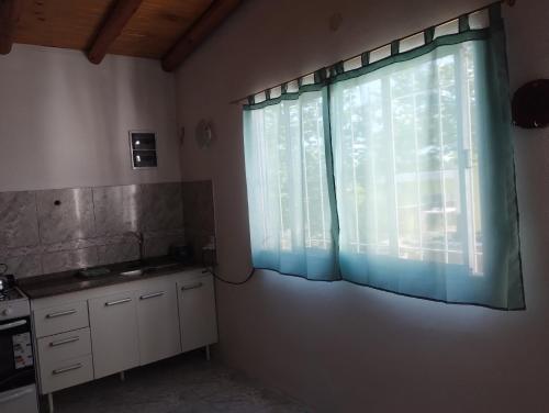 a kitchen with a large window with blue curtains at Atardecer Serrano in Huerta Grande