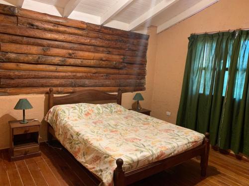 1 dormitorio con 1 cama y pared de madera en El Camino Viejo Cabañas en Villa General Belgrano