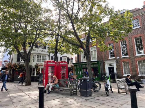 um homem sentado num banco ao lado de duas cabines telefónicas vermelhas em London Central Richmond Cozy Apartment em Richmond