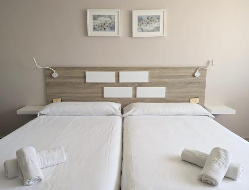 2 camas en un dormitorio con sábanas y almohadas blancas en Apartamentos Turísticos Guillermo, en Palas de Rei 