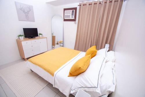 ein Schlafzimmer mit einem Bett mit gelben Kissen und einem TV in der Unterkunft Entire 1-Bedroom Condo in Makati in Manila