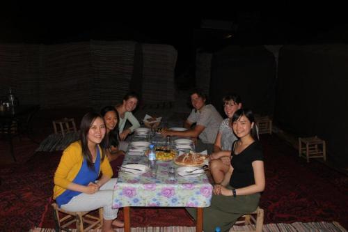 un grupo de personas sentadas alrededor de una mesa comiendo en Mirdane Camp, en Merzouga