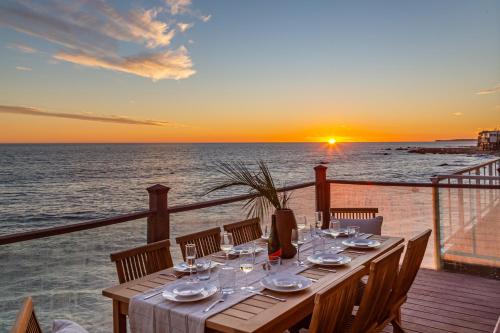 a table on a balcony with a sunset over the ocean at Blue Dolphin: An Oceanfront Malibu Sanctuary in Malibu