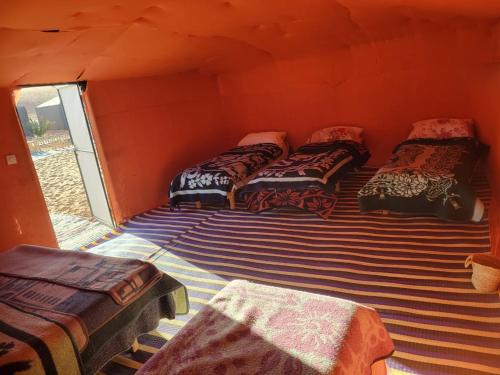 grupa łóżek w pokoju z pomarańczową ścianą w obiekcie Mirdane Camp w mieście Merzouga