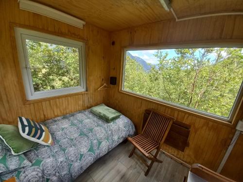a bedroom with a bed and a chair and two windows at Casa árbol Conguillio National Park in Melipeuco