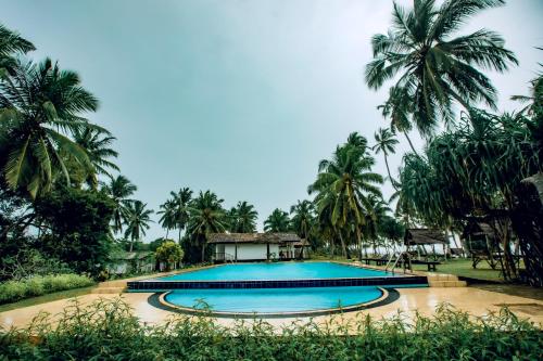 a swimming pool in front of a resort with palm trees at Helios Beach Resort in Tangalle