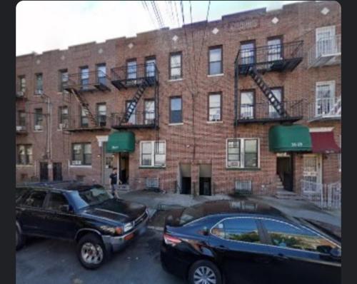 deux voitures garées devant un bâtiment en briques dans l'établissement Two bedroom excellent location, à Queens