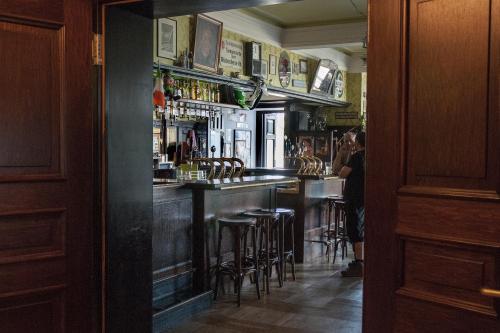 a bar with stools in a room with a man standing at a bar at Hajo´s Germania Lodge & Irish Pub in Rüdesheim am Rhein