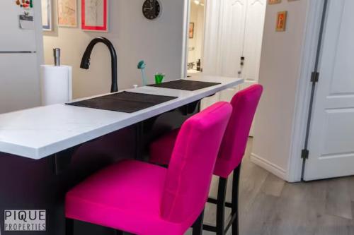 a kitchen with pink chairs at a kitchen island at The Neon Palace - KingBed - Fireplace - Netflix - UG Park in Edmonton