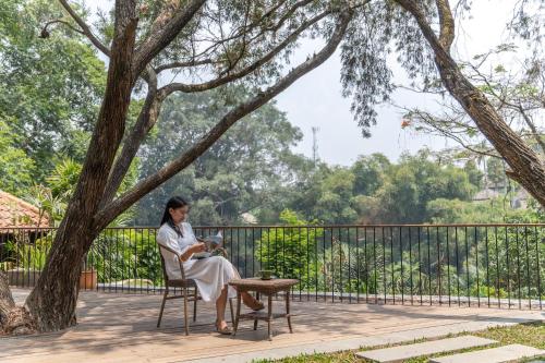 a woman sitting on a chair reading under a tree at Novus Giri Resort & Spa in Puncak