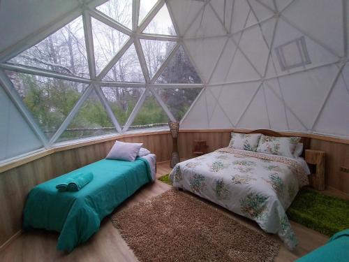 two beds in a room with a large window at CONCEPTO GLAMPING - DOMOS CONGUILLIO in Melipeuco