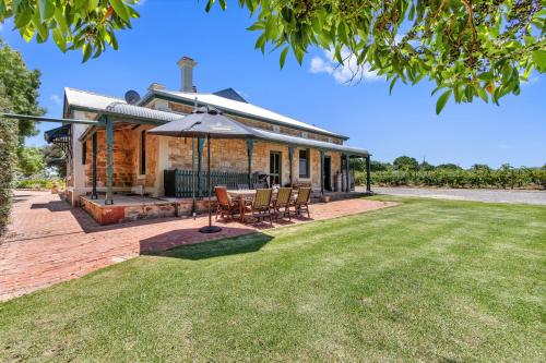 Barossa Vineyard Guesthouse في تانوندا: منزل به طاولة وكراسي ومظلة