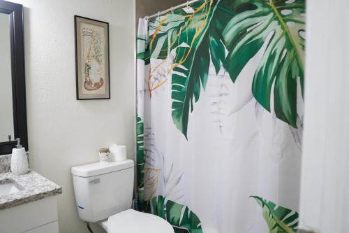 a bathroom with a toilet and a leafy shower curtain at Jay's Cozy Escape - A step from Busch Gardens in Tampa