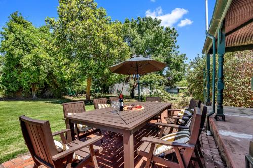Barossa Vineyard Guesthouse في تانوندا: طاولة خشبية مع كراسي ومظلة