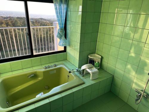 ein grünes Bad mit einer Badewanne und einem Fenster in der Unterkunft Mt.Fuji Rising Sun Inn in Fuji