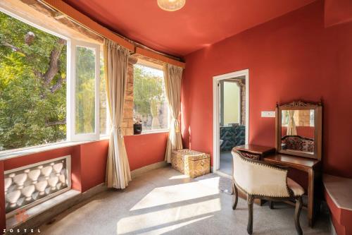 a red room with a chair and a desk and windows at Zostel Jodhpur (Ratanada) in Jodhpur