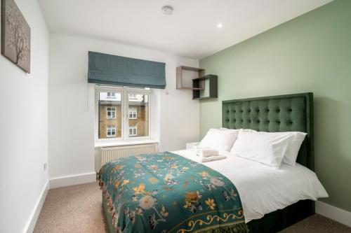 a bedroom with a bed with a green headboard and a window at Stunning 3BD Flat Free Parking close to Greenwich in London