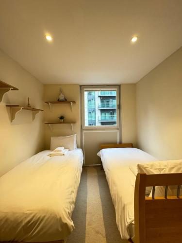 two beds in a small room with a window at Contemporary 2BD Flat wBalcony Canary Wharf! in London