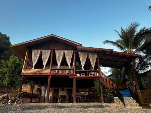 a wooden house with a balcony and a palm tree at พาราไดซ์รีสอร์ต สังขละบุรี Paradise Resort at Sangkhlaburi in Sangkhla Buri