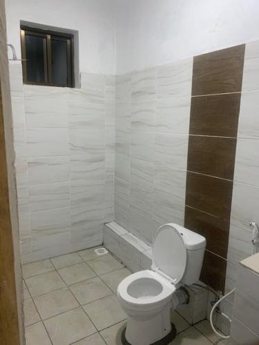 La salle de bains blanche est pourvue de toilettes et d'une fenêtre. dans l'établissement Wembley villla diani beach, à Diani Beach