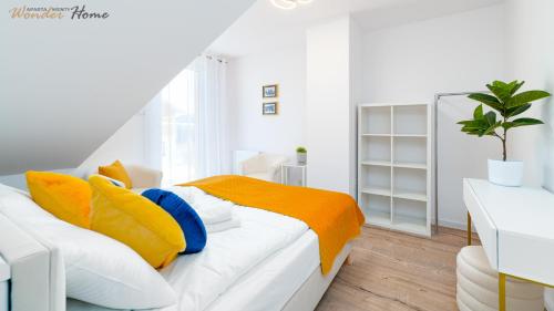 a white bedroom with yellow and blue pillows on a bed at Wonder Home - Apartamenty z widokiem na góry, blisko wyciągów, szlaków turystycznych i restauracji in Karpacz