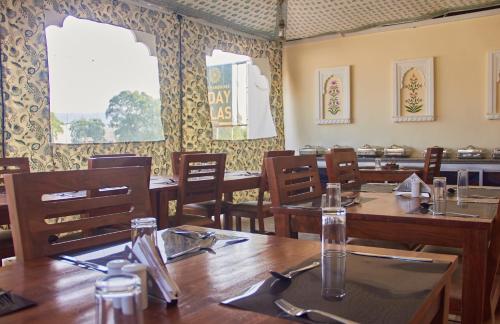 un restaurante con mesas y sillas de madera y ventanas en Ranthambhore Uday Vilas, en Sawāi Mādhopur