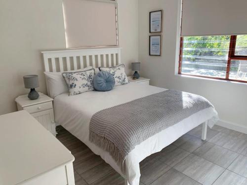 een slaapkamer met een wit bed met kussens en een raam bij Jay's Snug in Knysna