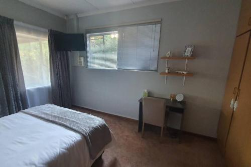 a bedroom with a bed and a desk and a window at Stay at the Ridge in Bloemfontein