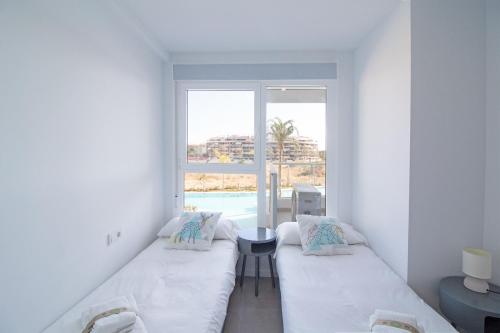 Habitación blanca con 2 camas y ventana en Global Properties, Apartamento para 5 personas con terraza y vistas a la piscina, en Canet de Berenguer