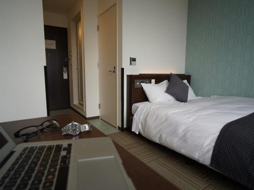 a bedroom with a bed and a desk with a laptop at Hotel New Gaea Domemae in Fukuoka