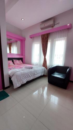 a pink bedroom with a bed and a black chair at Mami Hotel in Solok
