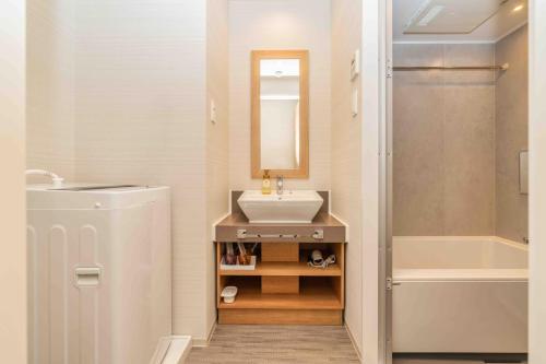 a bathroom with a sink and a mirror and a tub at Apartment Hotel 11 Namba in Osaka
