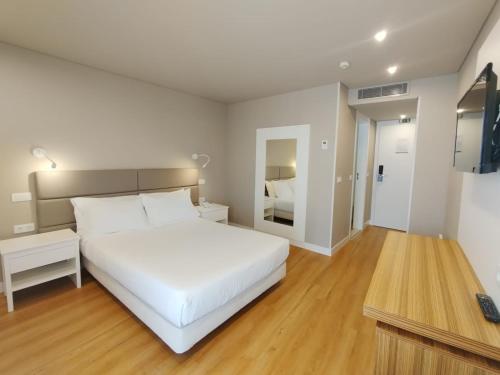 Biała sypialnia z białym łóżkiem i biurkiem w obiekcie Hotel Cristal Caldas w mieście Caldas da Rainha