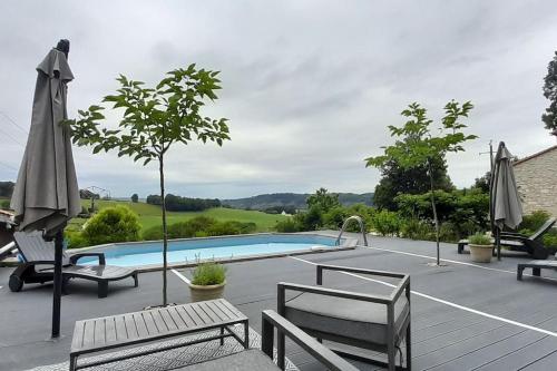 a swimming pool with chairs and umbrellas on a patio at Villa avec piscine chauffée Périgord Dordogne in Marnac