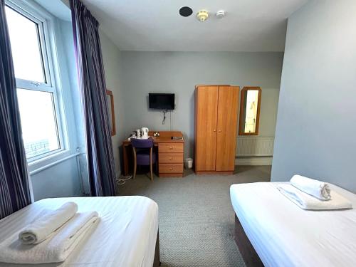 a room with two beds and a desk and a window at The Seafront Hotel by Compass Hospitality in Llandudno