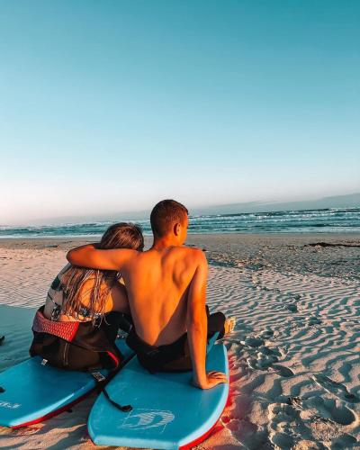 a man and a woman sitting on a surfboard on the beach at The Log House in Pearly Beach