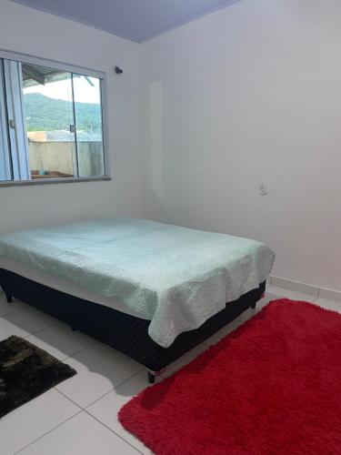 a bed in a white room with a red rug at Casa 01,02 in Bombinhas