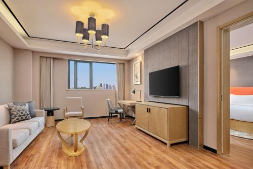 a hotel room with a couch and a bed and a television at Hilton Garden Inn Wuhan Hankou in Wuhan