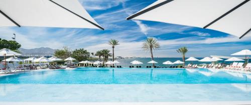 een groot zwembad met witte parasols en de oceaan bij Crowne Plaza Muscat, an IHG Hotel in Muscat