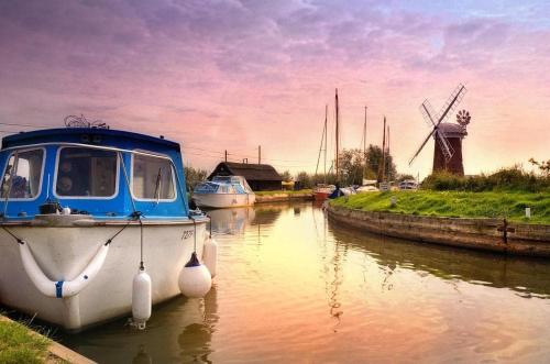 a boat is docked in a canal with a windmill at 194, Belle Aire, Hemsby - Two bed recently renovated chalet, sleeps 4, pet friendly, free Wi-Fi and bed linen and towels included in Hemsby