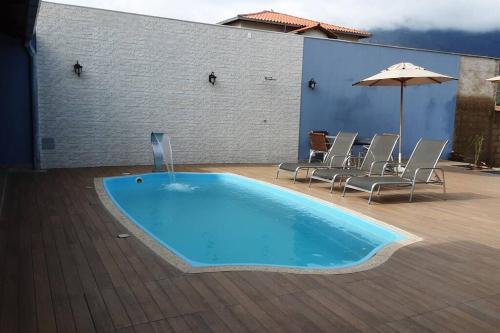 a swimming pool with chairs and an umbrella at Espaço Dunei - Casa inteira com piscina in Catas Altas