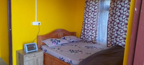 um quarto com uma cama e uma parede amarela em Teesta Stay & Restaurant em Darjeeling