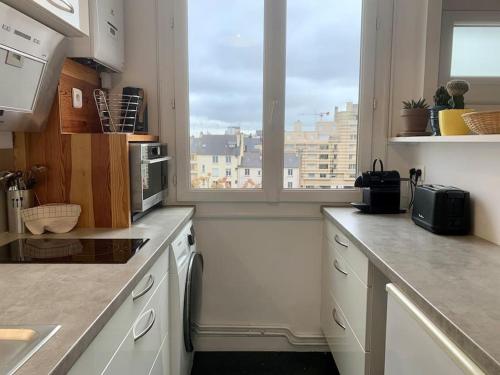 une cuisine avec des placards blancs et une vue sur la ville dans l'établissement Le Saint HeL, Magnifique T2 en face du TNB, à Rennes