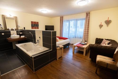 a bathroom with a bath tub and a living room at Haller's Posthotel in Riezlern